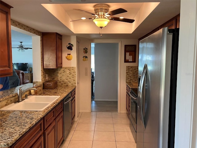 kitchen with appliances with stainless steel finishes, a tray ceiling, backsplash, ceiling fan, and light tile floors