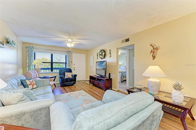 living room featuring light hardwood / wood-style floors, ceiling fan, and a textured ceiling