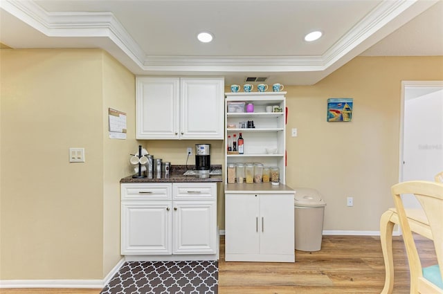 interior space with ornamental molding, white cabinetry, dark stone counters, and light hardwood / wood-style flooring