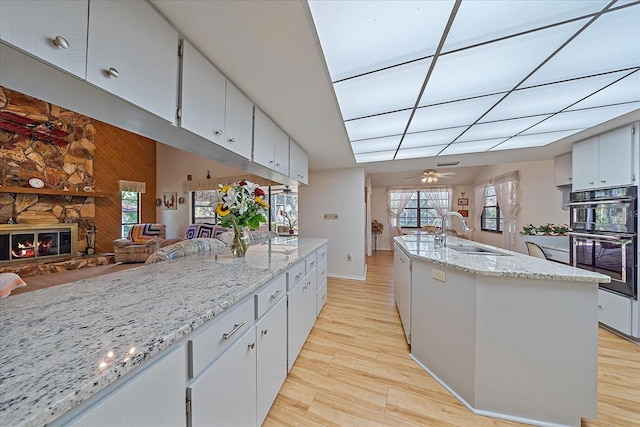 kitchen with double oven, a fireplace, light stone countertops, and a center island with sink