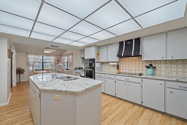 kitchen featuring sink, tasteful backsplash, black appliances, a kitchen island with sink, and exhaust hood