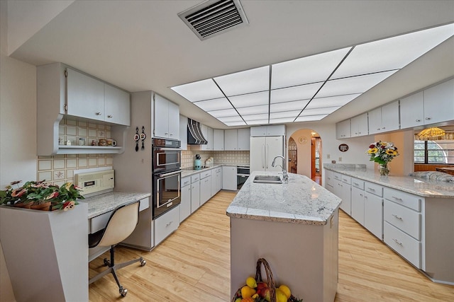 kitchen with built in fridge, sink, light wood-type flooring, and wall chimney exhaust hood