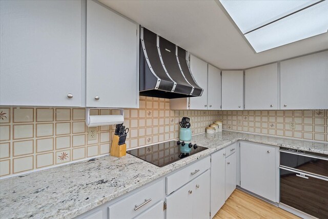 kitchen featuring light hardwood / wood-style flooring, white cabinetry, black electric stovetop, decorative backsplash, and exhaust hood