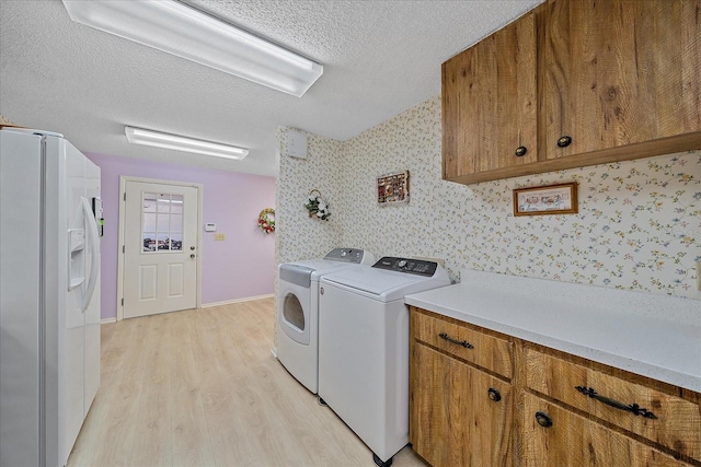 clothes washing area featuring light hardwood / wood-style flooring, washer and clothes dryer, cabinets, and a textured ceiling