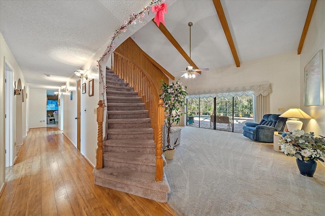 stairs featuring ceiling fan, hardwood / wood-style flooring, lofted ceiling with beams, and a textured ceiling