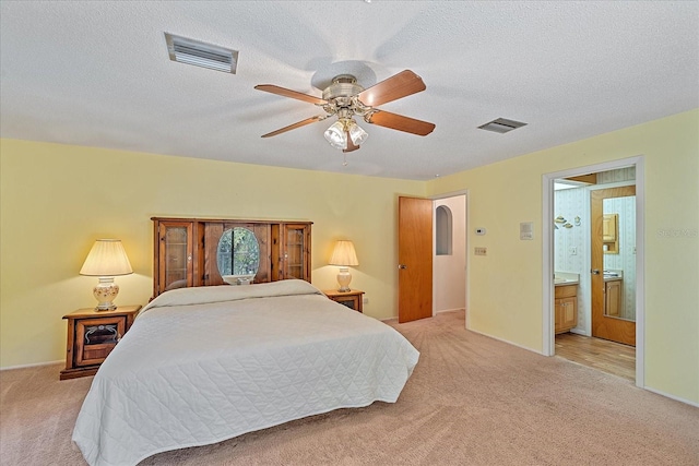 bedroom featuring light carpet, ceiling fan, a textured ceiling, and ensuite bathroom