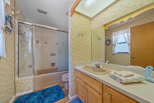 full bathroom with vanity, hardwood / wood-style floors, shower / bath combination with glass door, and toilet