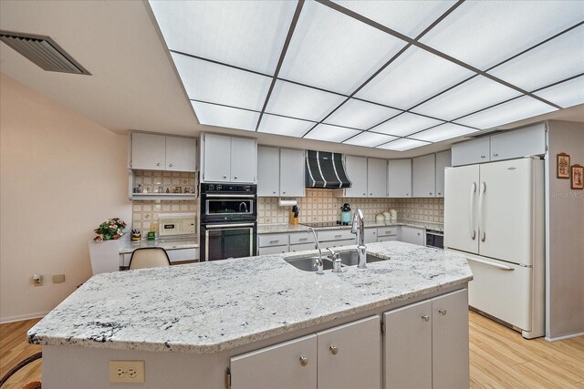 kitchen featuring decorative backsplash, black appliances, wall chimney exhaust hood, and a center island with sink