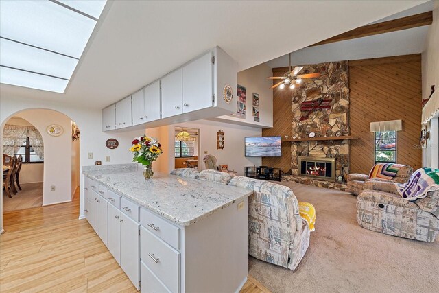 kitchen with a stone fireplace, wood walls, white cabinetry, high vaulted ceiling, and light stone countertops