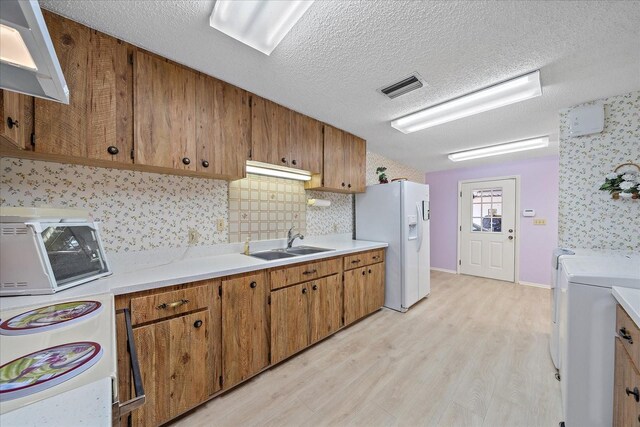 kitchen featuring sink, tasteful backsplash, light hardwood / wood-style floors, white fridge with ice dispenser, and a textured ceiling