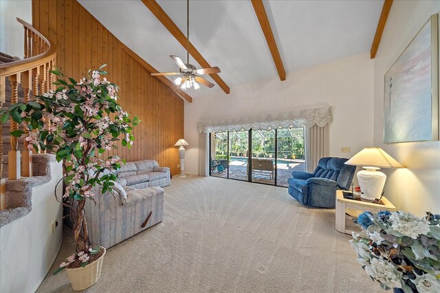 carpeted living room with beamed ceiling, ceiling fan, high vaulted ceiling, and wood walls