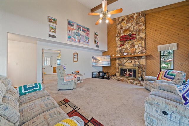 living room featuring a stone fireplace, carpet flooring, high vaulted ceiling, and wooden walls