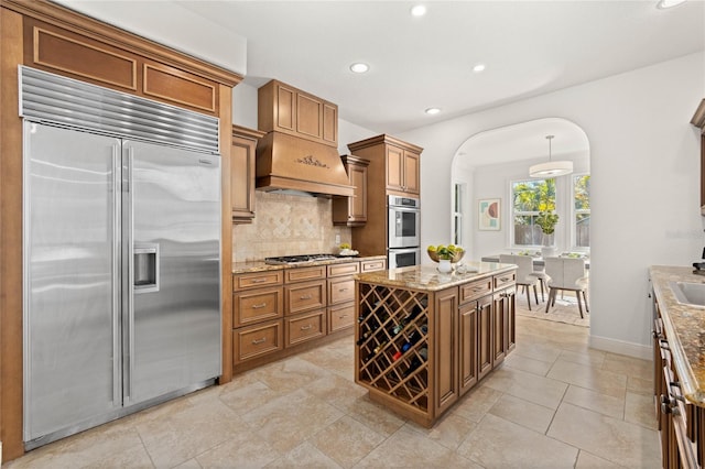 kitchen featuring light stone countertops, hanging light fixtures, stainless steel appliances, backsplash, and a kitchen island