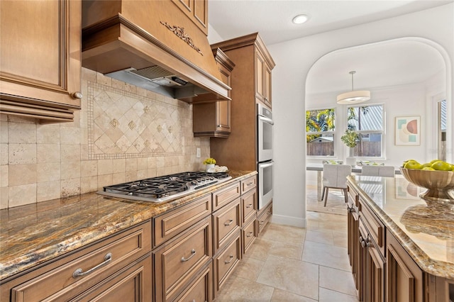 kitchen with tasteful backsplash, premium range hood, stainless steel appliances, and dark stone countertops