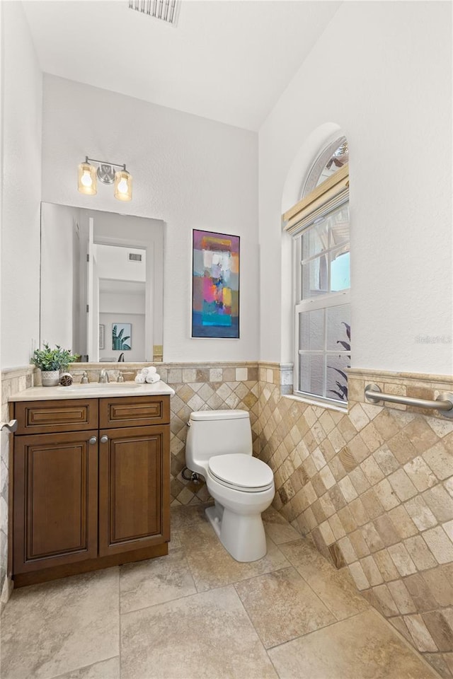 bathroom featuring tile patterned flooring, vanity, toilet, and tile walls