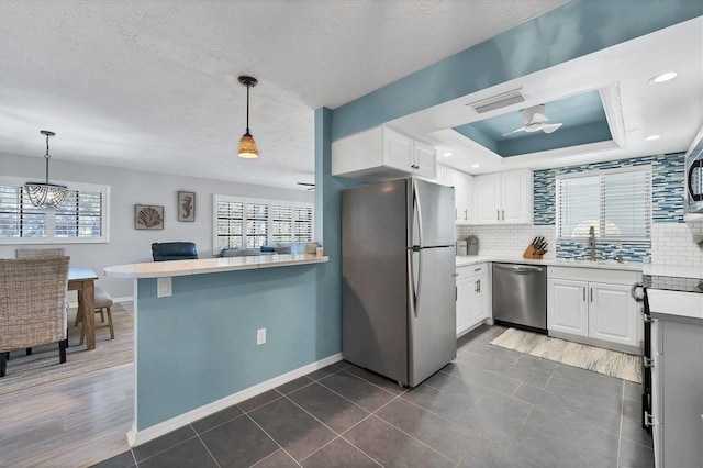 kitchen with white cabinets, appliances with stainless steel finishes, decorative light fixtures, and tasteful backsplash