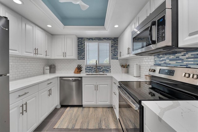 kitchen featuring stainless steel appliances, a sink, white cabinetry, decorative backsplash, and a tray ceiling