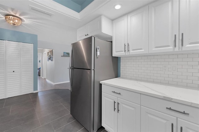 kitchen with tasteful backsplash, white cabinetry, stainless steel fridge, dark tile floors, and light stone counters