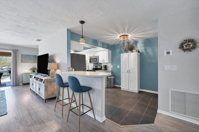 kitchen with white cabinetry, backsplash, a kitchen breakfast bar, appliances with stainless steel finishes, and pendant lighting