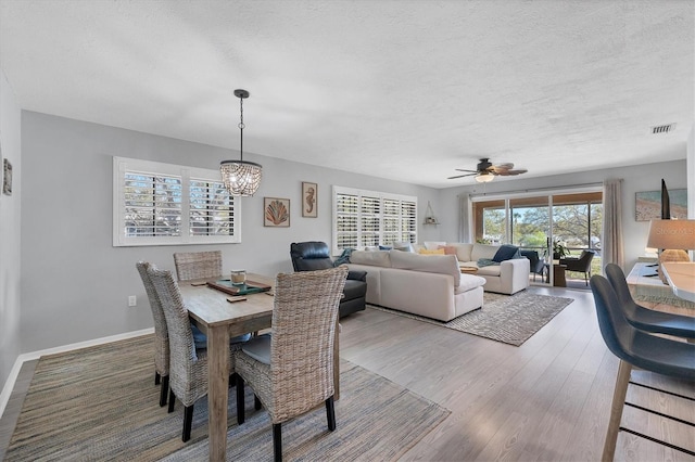 dining space featuring a textured ceiling, ceiling fan with notable chandelier, and light wood-type flooring