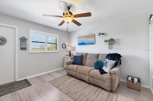 living room with a barn door, light hardwood / wood-style floors, and ceiling fan