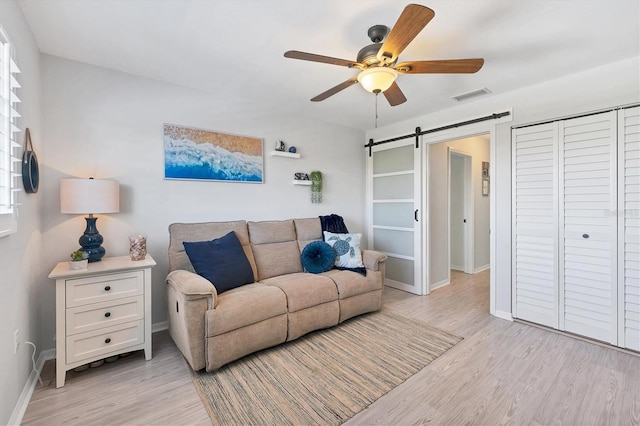 living room featuring a barn door, light hardwood / wood-style floors, and ceiling fan