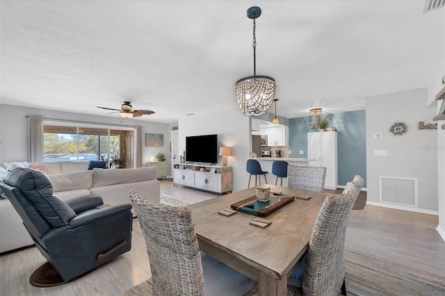 dining room with ceiling fan with notable chandelier and light hardwood / wood-style flooring