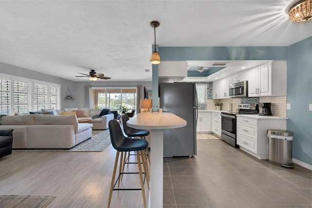 kitchen with hanging light fixtures, backsplash, ceiling fan with notable chandelier, appliances with stainless steel finishes, and white cabinets