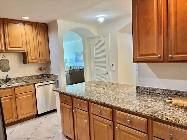 kitchen with light tile floors, stone counters, stainless steel dishwasher, and sink