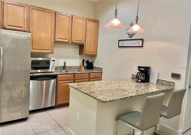 kitchen with light stone countertops, appliances with stainless steel finishes, a breakfast bar, light tile floors, and pendant lighting