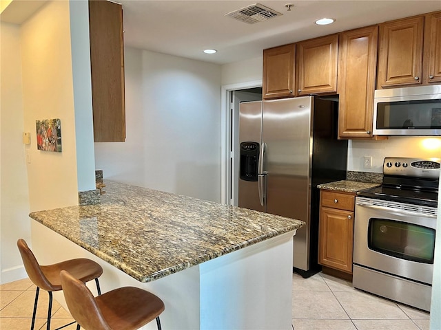 kitchen with kitchen peninsula, a breakfast bar, stainless steel appliances, dark stone countertops, and light tile floors