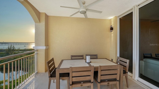 balcony at dusk featuring ceiling fan and a water view