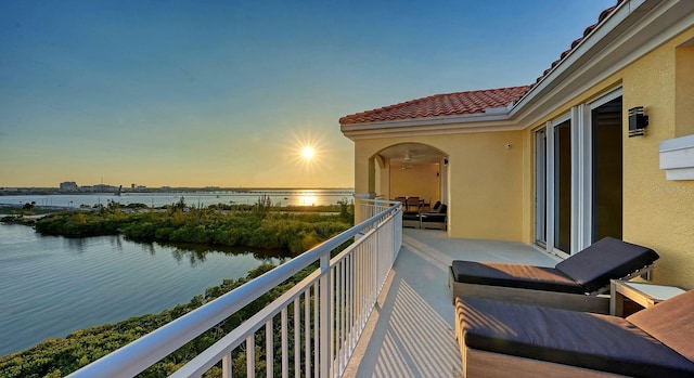 balcony at dusk featuring a water view