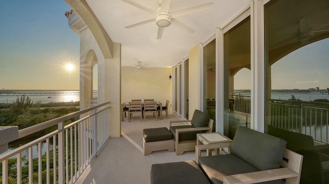 balcony at dusk with ceiling fan and a water view