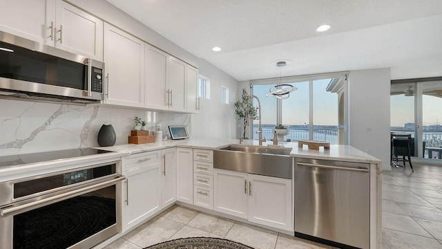 kitchen featuring appliances with stainless steel finishes, sink, white cabinets, light stone counters, and a water view