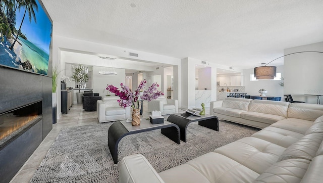 living room featuring a glass covered fireplace, visible vents, concrete floors, and a textured ceiling