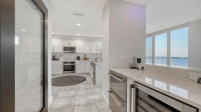 kitchen with tasteful backsplash, stainless steel appliances, wine cooler, white cabinets, and light stone countertops