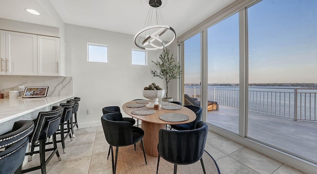 dining space featuring light tile patterned flooring, a chandelier, and a water view