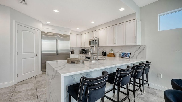 kitchen featuring tasteful backsplash, visible vents, light stone counters, appliances with stainless steel finishes, and a peninsula