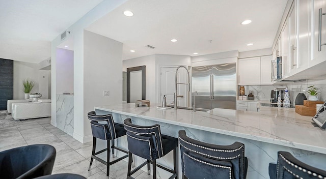 kitchen featuring a kitchen bar, kitchen peninsula, stainless steel appliances, light stone countertops, and white cabinets