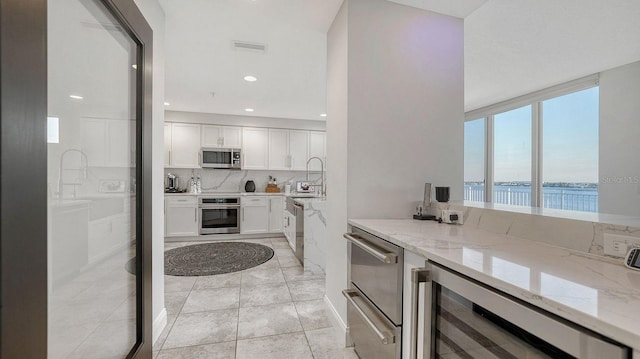 kitchen with white cabinetry, stainless steel appliances, a water view, light stone counters, and wine cooler