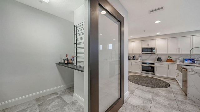 kitchen featuring white cabinetry, backsplash, light tile patterned floors, stainless steel appliances, and light stone countertops