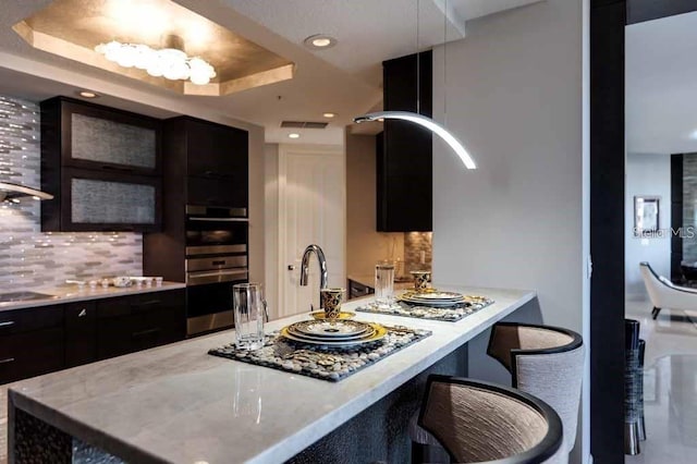 kitchen featuring a kitchen bar, backsplash, a tray ceiling, and double oven