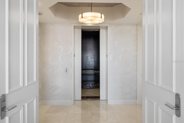 hallway with baseboards, a raised ceiling, and light tile patterned flooring