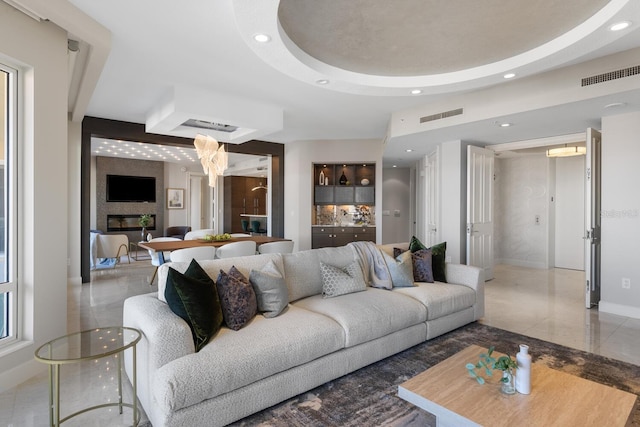 living area with visible vents, recessed lighting, a raised ceiling, and baseboards