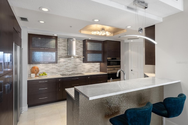 kitchen featuring black electric stovetop, wall chimney range hood, double oven, a peninsula, and a sink