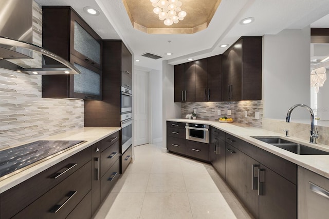 kitchen with visible vents, black electric stovetop, wall chimney exhaust hood, a raised ceiling, and a sink