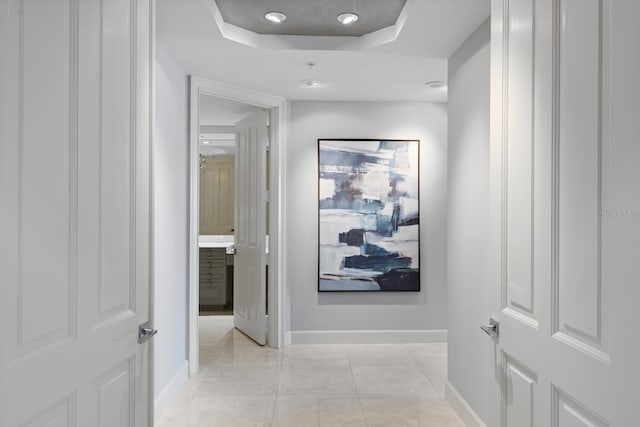 hallway with light tile patterned floors, baseboards, and a tray ceiling