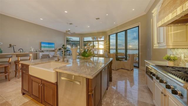 kitchen featuring ceiling fan, sink, a kitchen island with sink, backsplash, and light stone countertops