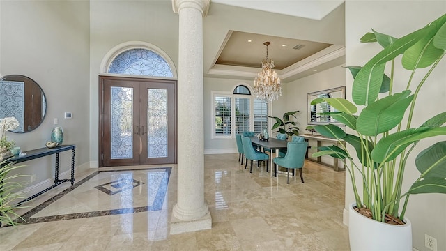 entryway with an inviting chandelier, a raised ceiling, a high ceiling, french doors, and ornate columns